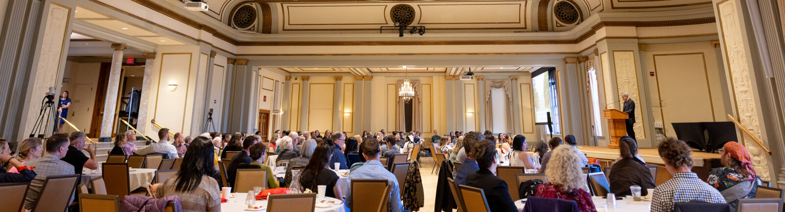 Group of people sitting at tables listening to someone speaking.