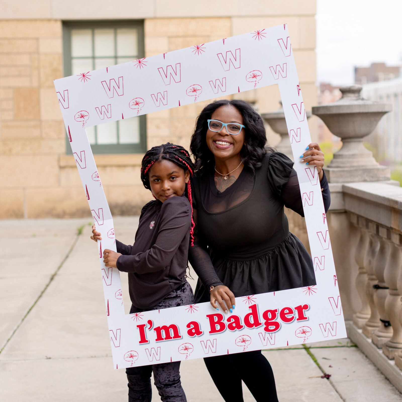 Returning adult student and daughter looking through a frame that reads, "I'm a Badger."