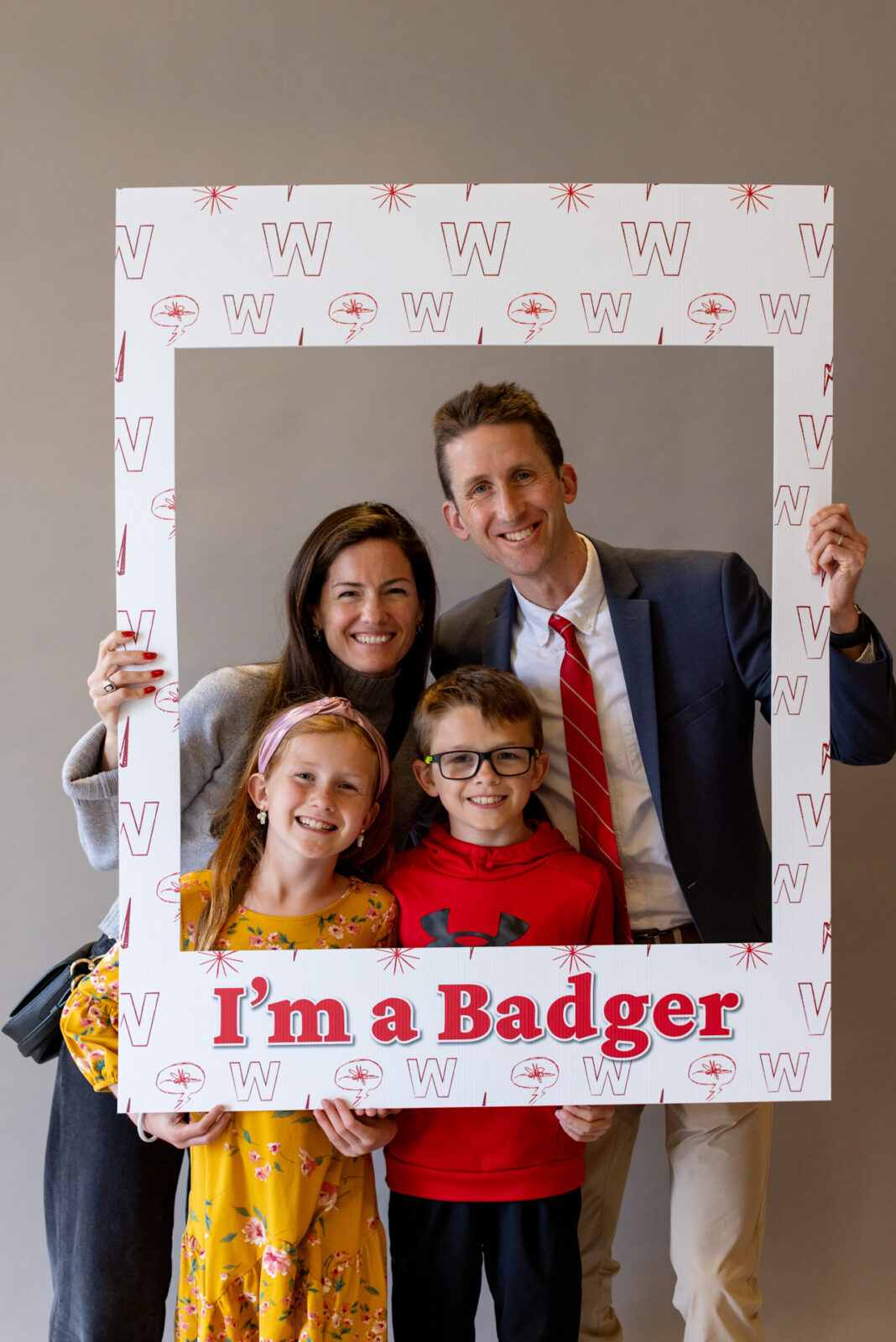 Returning adult student with his family, all looking through a frame that reads, "I'm a Badger."