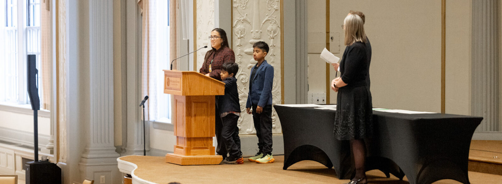 Returning adult student with children on stage receiving certificate.